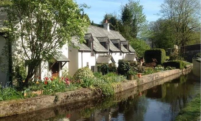 Canal side scenic view as the horse drawn boat travels a long the Llangollen canal edged by trees, foilage and flowers surrounding the canal side cott